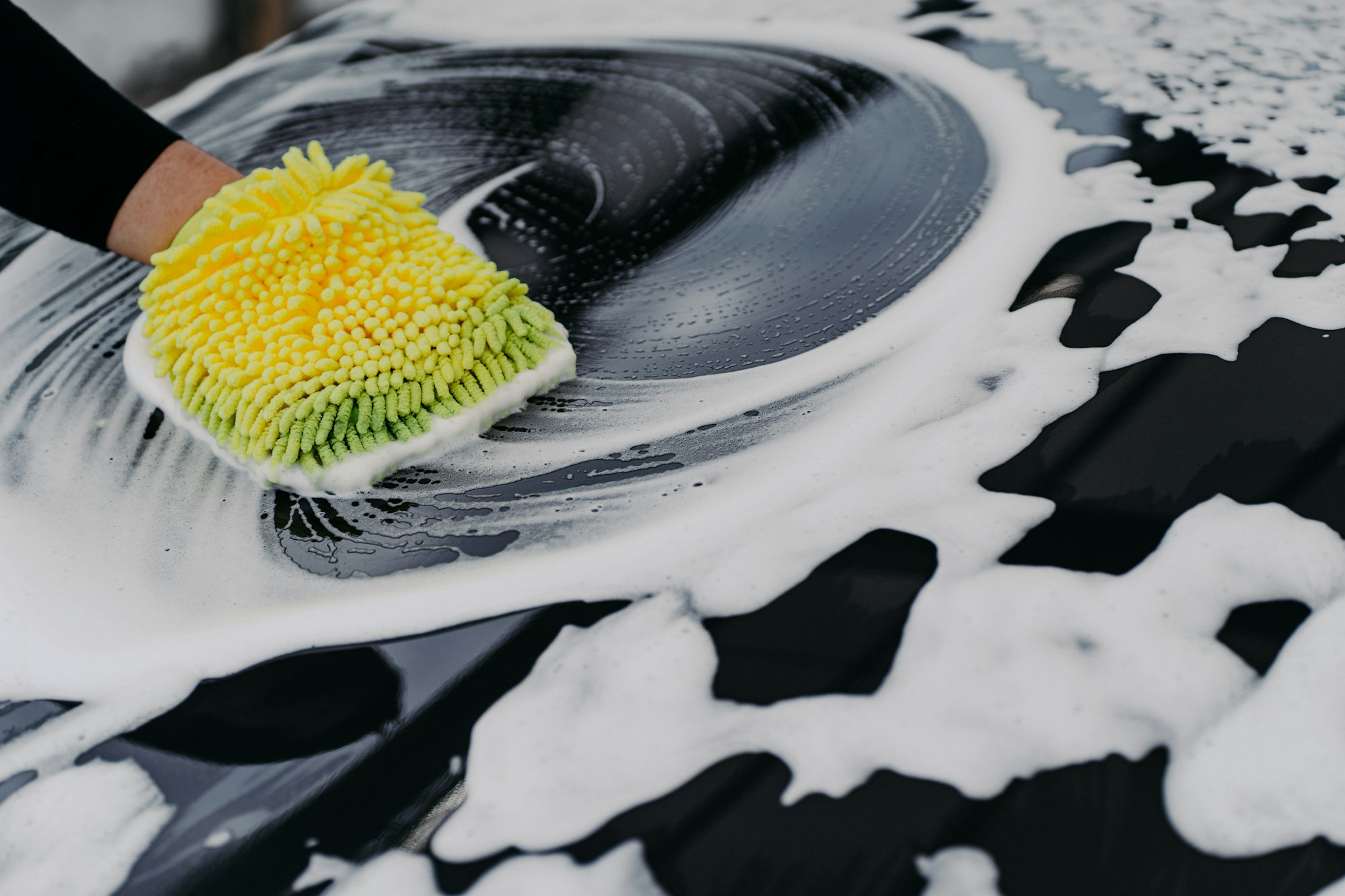 Mans hand washing black car with cloth and soap bubbles. Cleaning automobile.